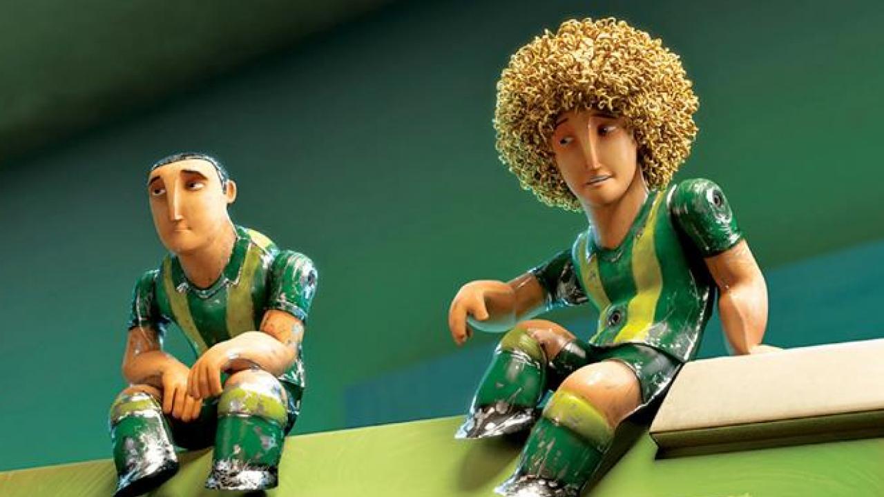 Zwei Tischfußballfiguren in grünen Trikots sitzen auf einer Tischkante, eine mit Locken, die andere mit kurzen Haaren