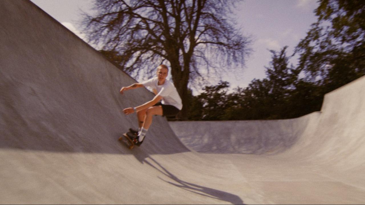 Totale einer jungen, kurzhaarigen Frau, die auf ihrem Skateboard in einer Halfpipe fährt.