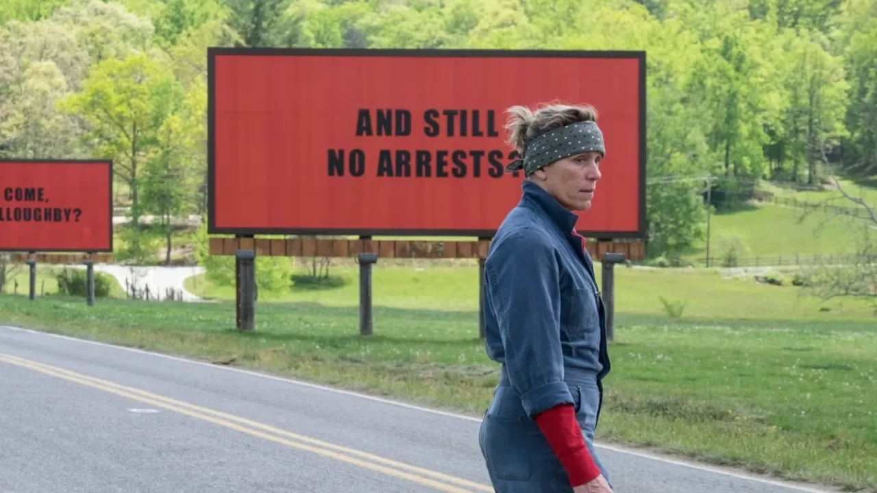 Frau in Overall steht auf Straße vor rotem Plakat mit der Aufschrift „AND STILL NO ARRESTS“.