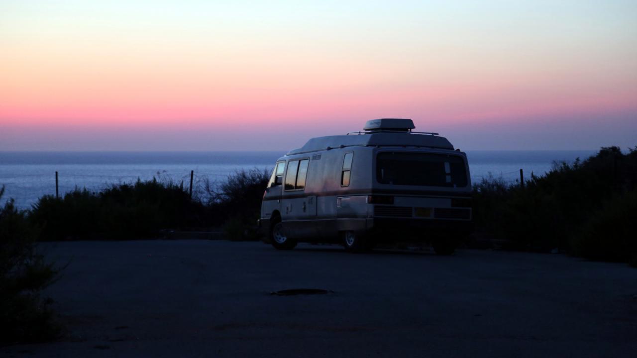 Szenenbild aus dem Roadmovie ROADS: Ein Campervan steht im Sonnenuntergang am Meer.