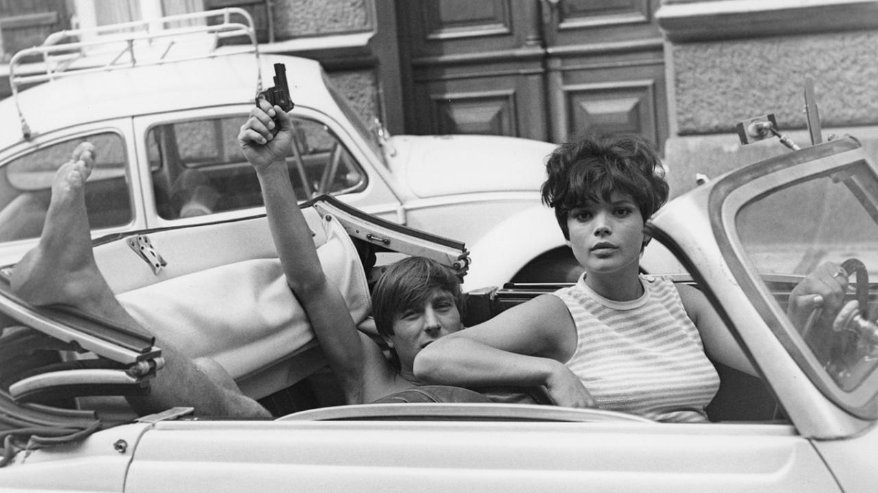 Martin (Werner Enke) und Barbara (Uschi Glas) in einem VW-Käfer-Cabrio. Werner mt nacktem Oberkörper sitzt hinten und hält einen Revolver in die Höhe.