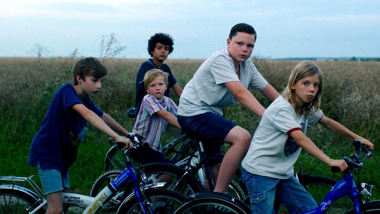 Szenenbild aus dem Film KÖNIGIN VON NIENDORF: Fünf Jungs auf Fahrräder sind an einem Feld angehalten und gucken auf ihrer rechten Seite.