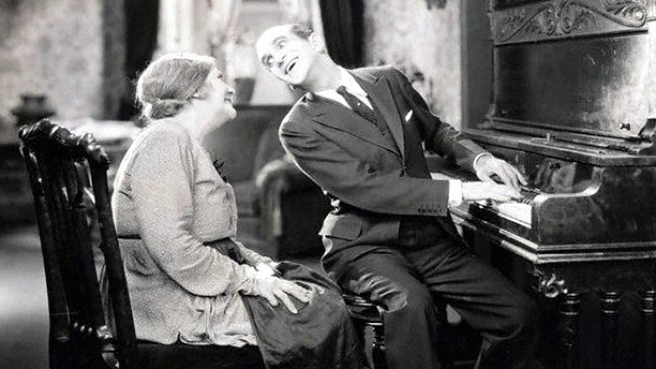 Szenenbild aus dem Film THE JAZZ SINGER (1927): Ein Klavierspieler singt ein Lied für eine ältere Frau.