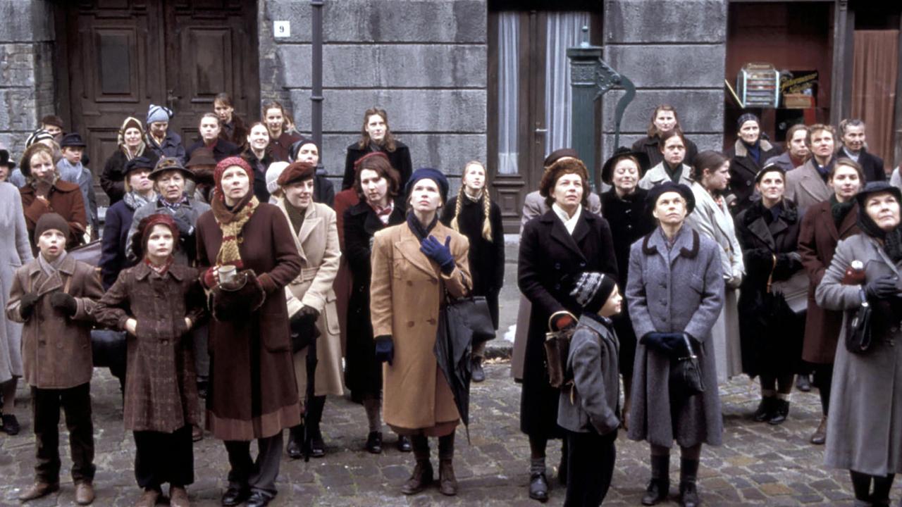 Szenenbild  aus dem Drama ROSENSTRASSE: Frauen und Kinder, gekleidet im Stil der 1940er-Jahre stehen vor einem Haus und schauen nach oben.