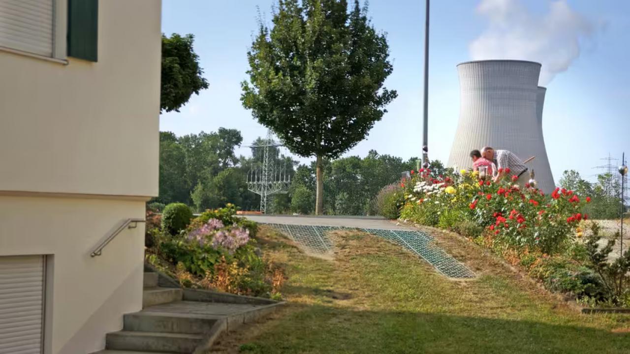 Atomkraft Forever, Szenenbild: Ein Vorgarten eines Hauses in Grundremmingen, im Hintergrund Kühltürme des Atomkraftwerks)