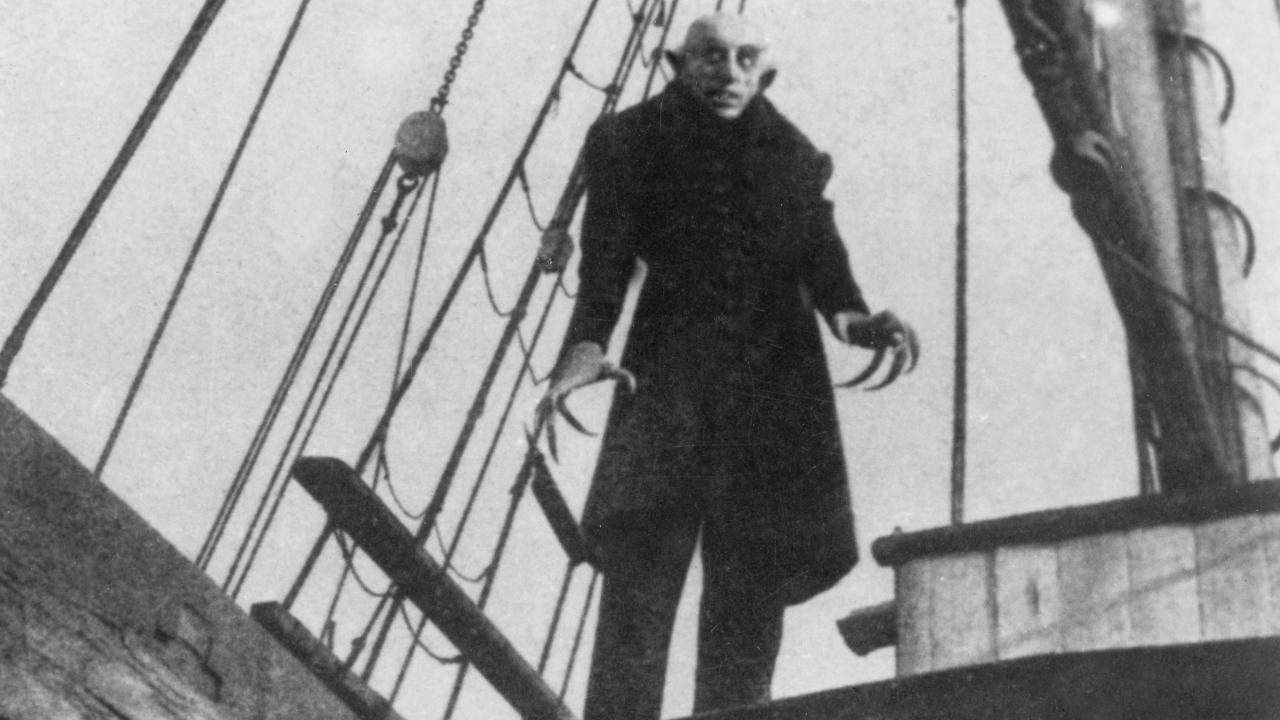 Szenenbild aus dem Stummfilm NOSFERATU – EINE SYMPHONIE DES GRAUENS: Ein unheimlicher Mann mit krallenartigen Fingern steht auf dem Deck eines Segelschiffs 