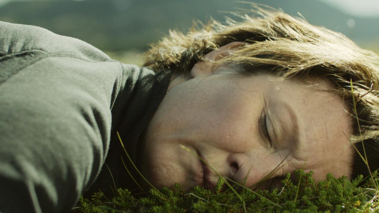 Gegen den Strom, Szenenbild: Nahaufnahmer einer Frau um die 50 mit kurzen Haaren, die wie schlafend auf Gras liegt.