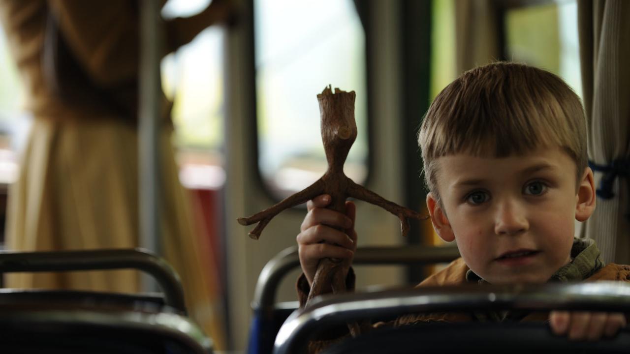 Mein Freund Knerten, Szenenbild: Ein Junge sitzt im Bus und hält eine Holzfigur in der Hand.