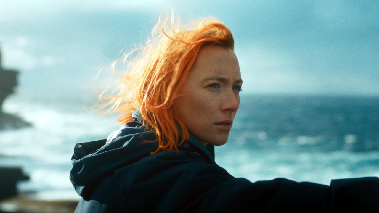 Szenenbild aus dem Drama THE OUTRUN: Porträt einer jungen Frau am Meer; ihre orangefarbenen Haare wehen im Wind.