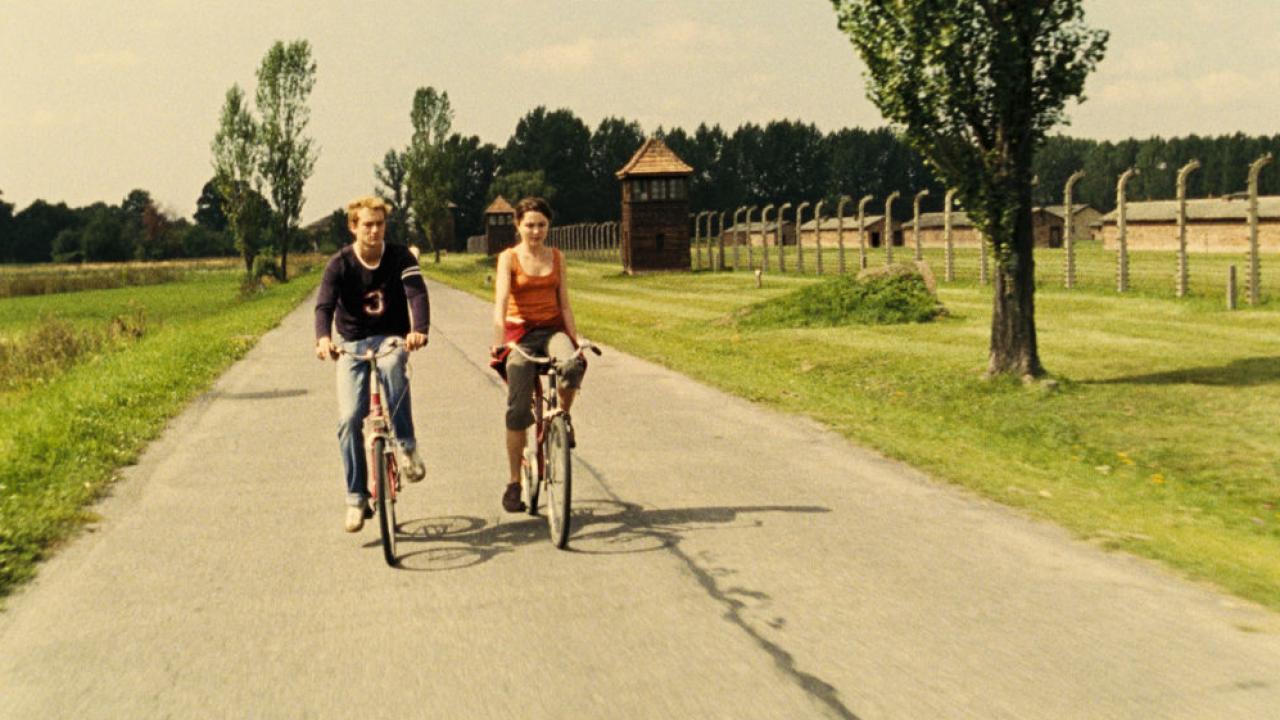 Am Ende kommen Touristen: ein Mann und eine Frau fahren Fahrrad auf einer ländlichen Straße. Auf der Seite der Straße ist ein Zaun.