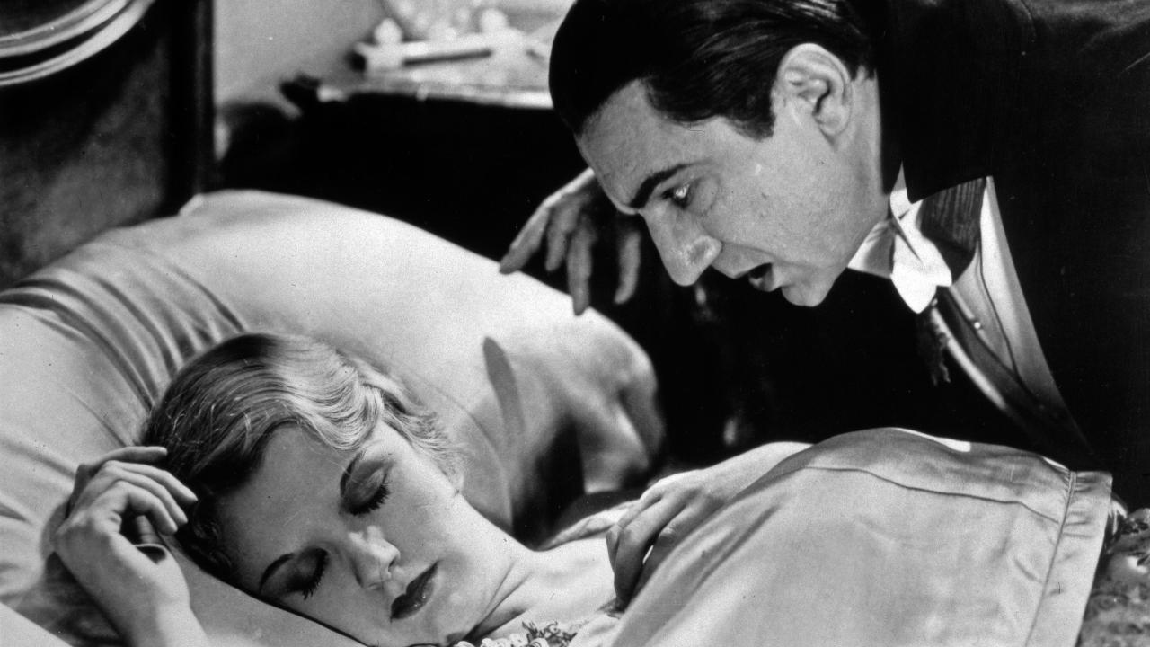 Szenenbild aus dem Film DRACULA (1931): In halbnaher Aufnahme beugt sich ein dunkelhaariger Mann im Smoking bedrohlich über eine im Bett schlafende blonde Frau.