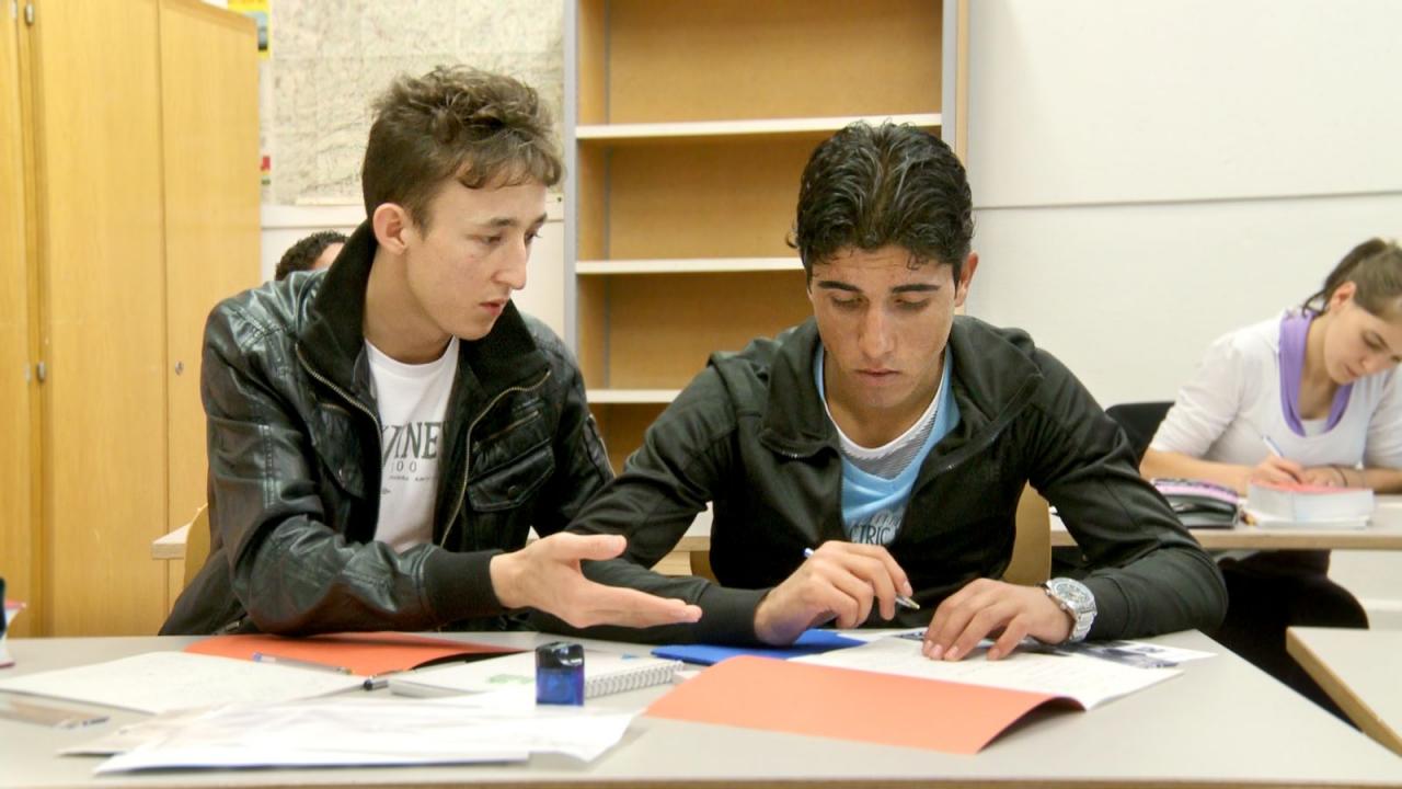 Neuland, Szenenbild: zwei junge Männer sitzen neben einander in einem Klassenzimmer.