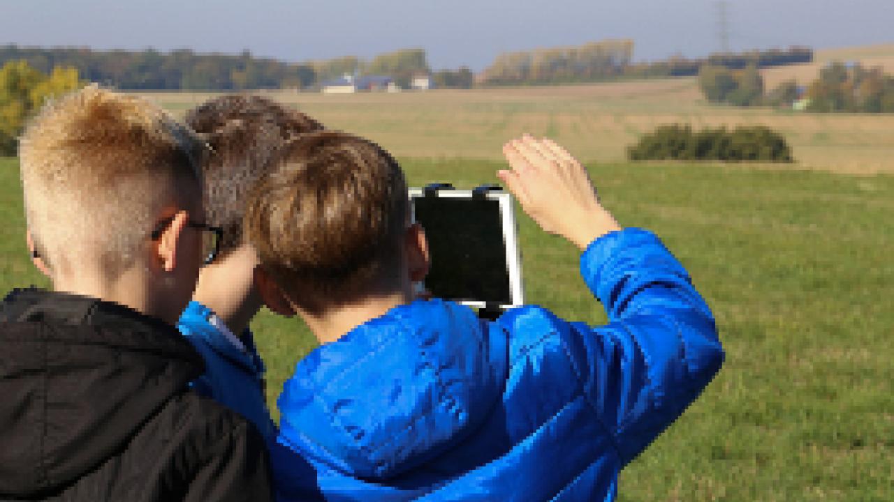 Drei Jungen, die am Projekt FILMmobil teilnehemn, filmen in einer ländlichen Landschaft mit einem Tablet