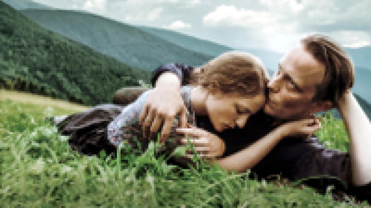 Ein verborgenes Leben, Szenenbild: Ein Mann und eine Frau liegen auf einer Wiese in den Bergen. Er hat seinen Arm um sie gelegt.