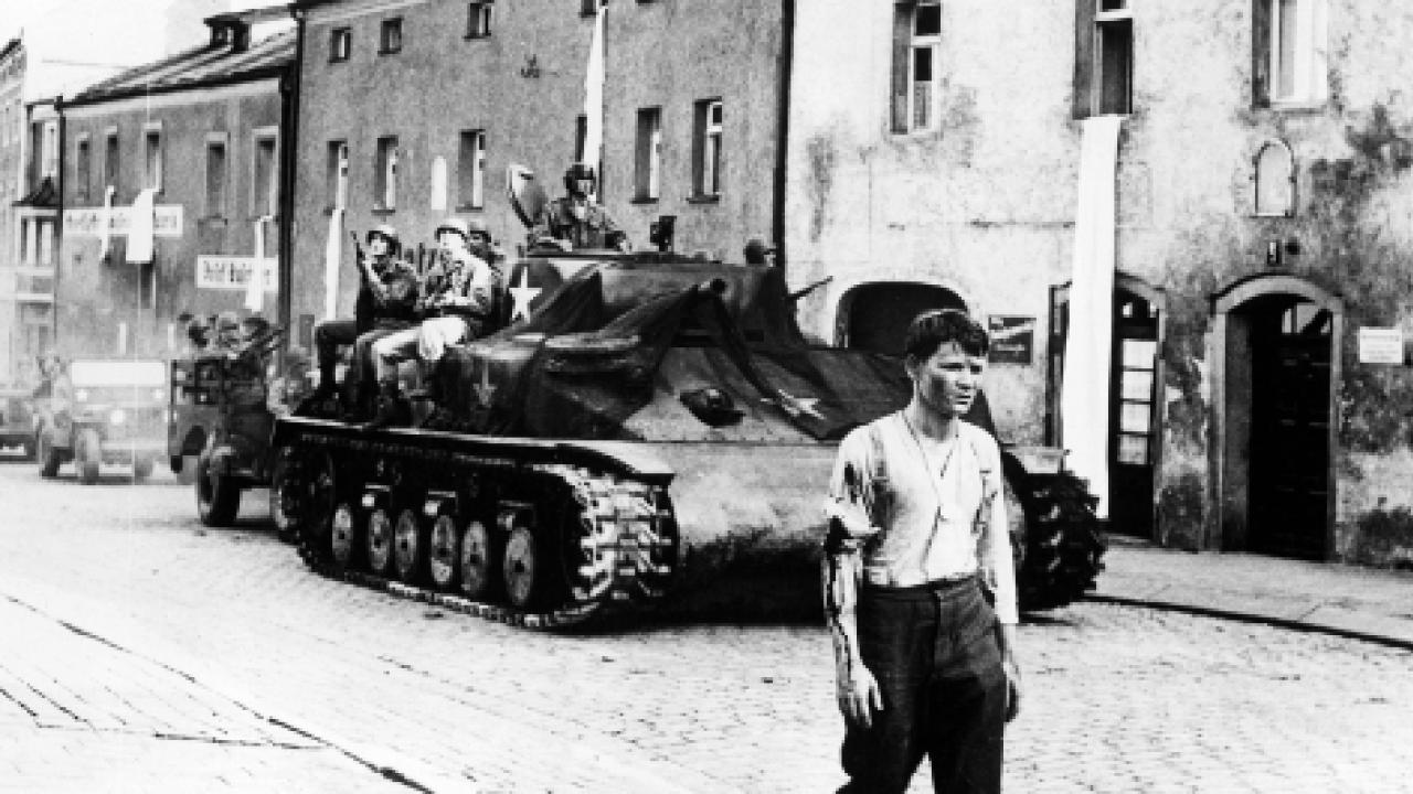 Die Brücke, Szenenbild: Ein junger Mann in Hemd und Uniformhose geht eine Straße entlang. Hinter ihm fährt ein Panzer.