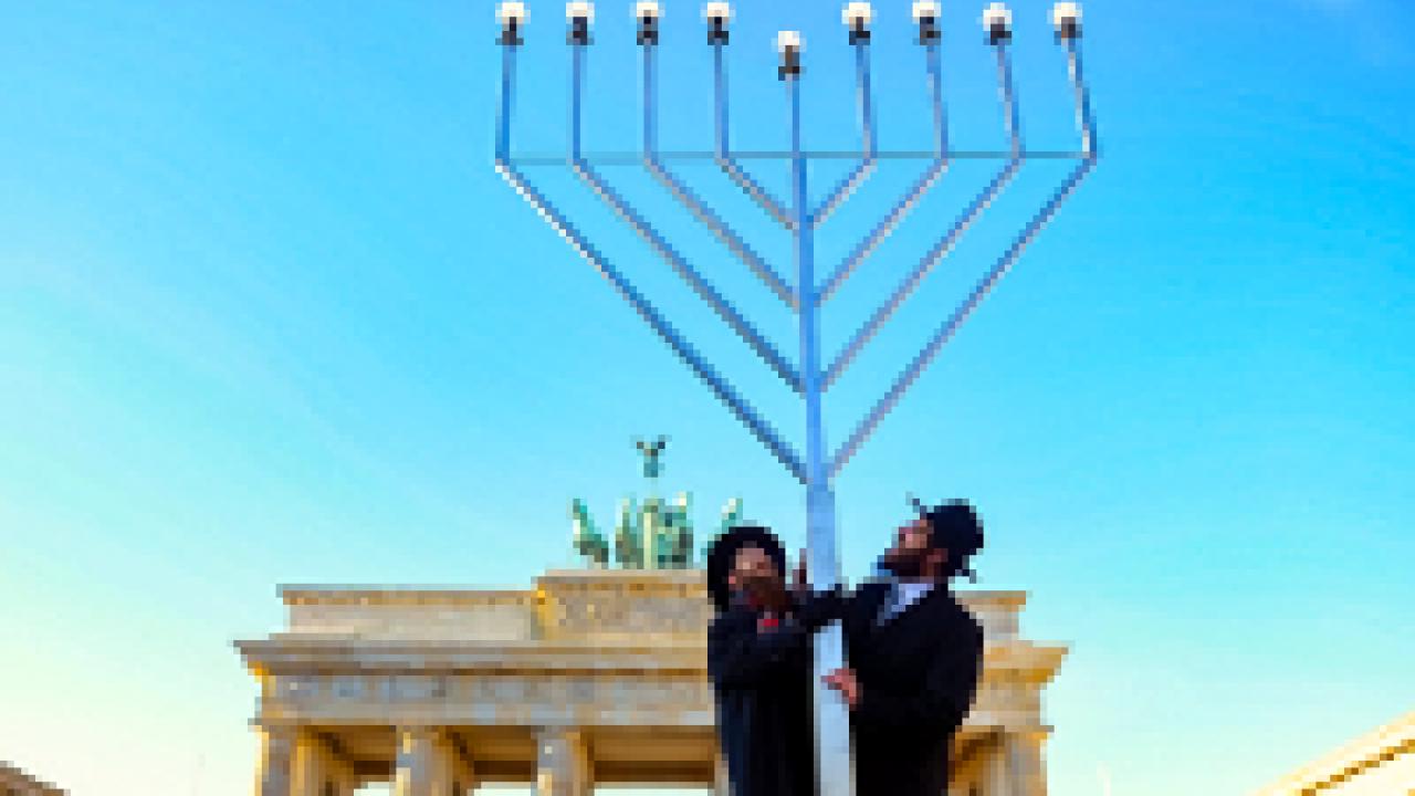 Germans & Jews, Szenenbild: Zwei jüdisch-orthodoxe Männer errichten in Berlin vor dem Brandenburger Tor einen riesigen Chanukka-Leuchter