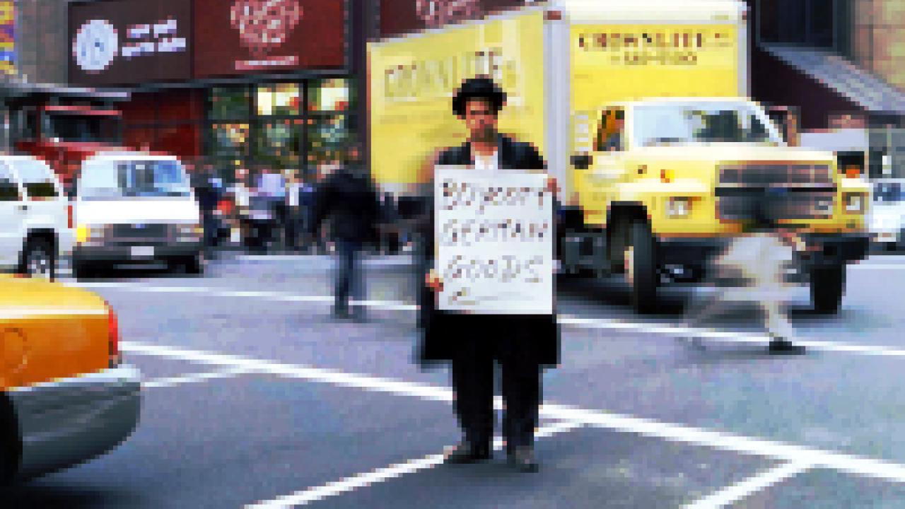 Schlingesief – In das Schweigen hineinschreien, Szenenbild: Ein Mann steht mit einem Protestschild auf einer belebten Straßenkreuzung in New York