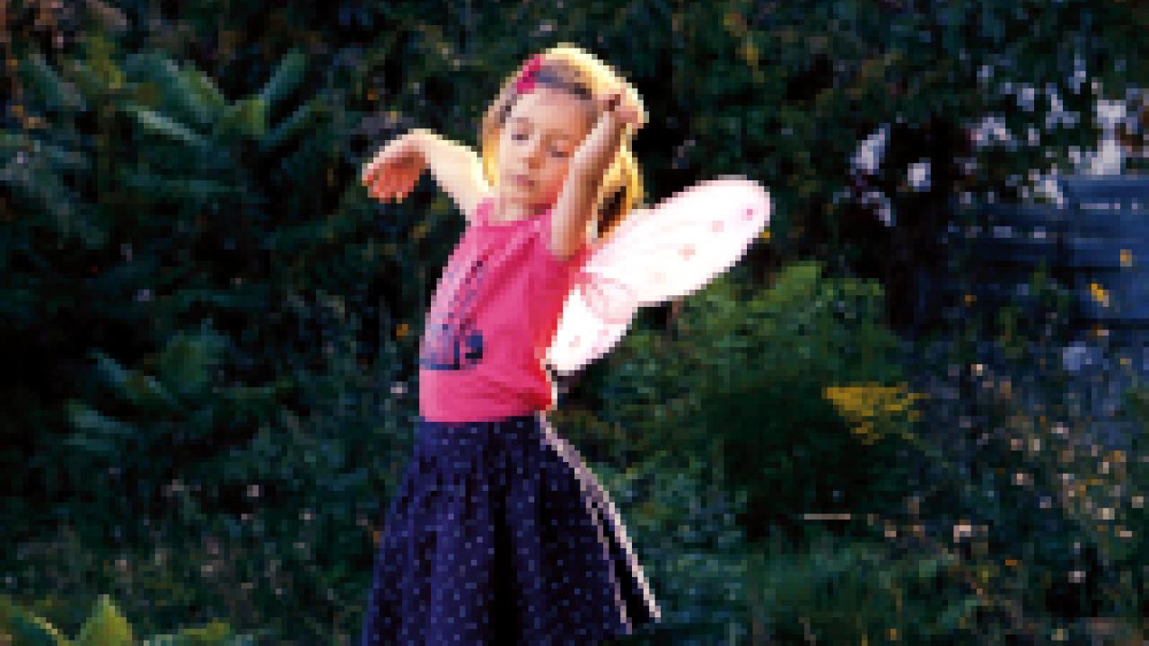 Kleines Mädchen, Szenenbild: Ein kleines Mädchen mit Schmetterlingsflügeln auf dem Rücken tanzt im Garten