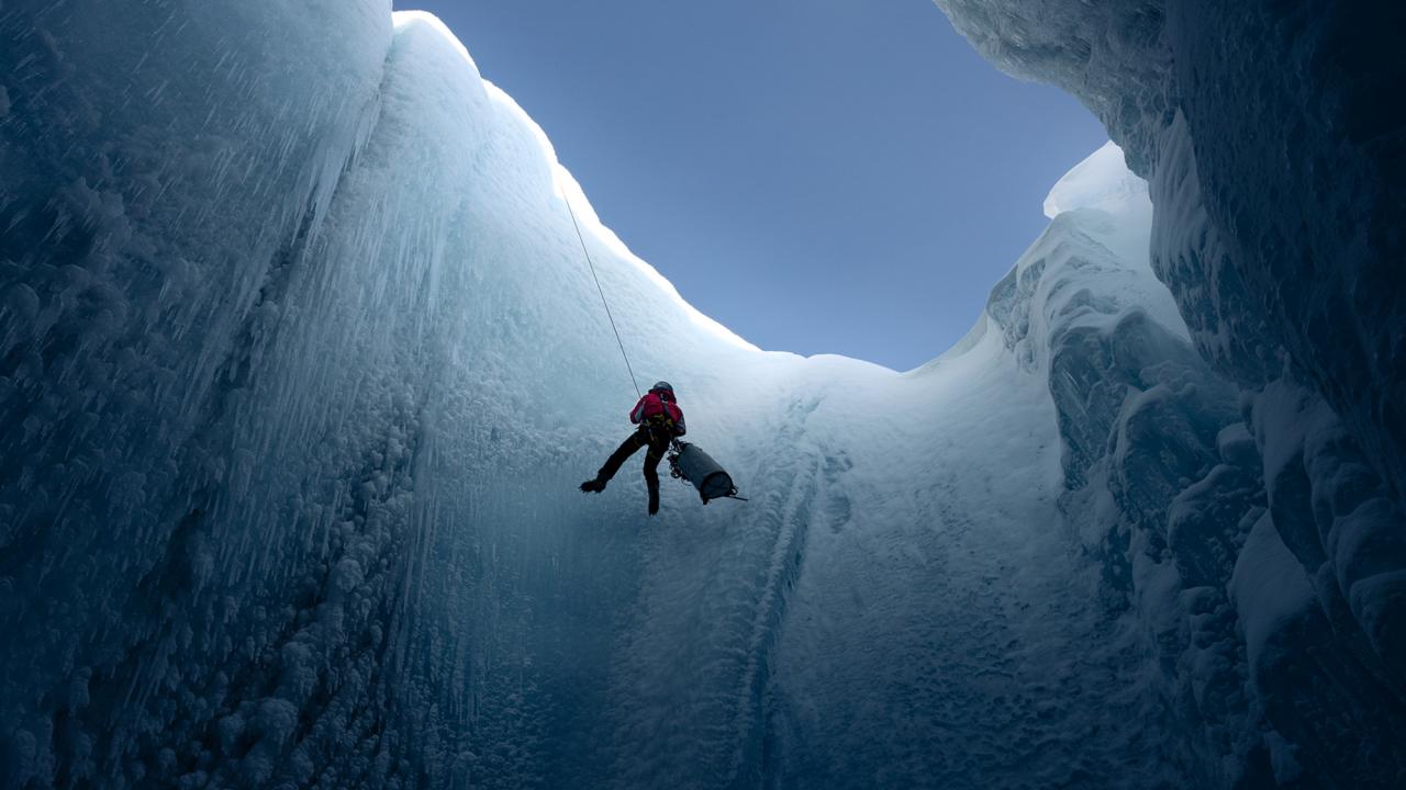 Into the Ice, Szenenbild: Totale eines Mannes, der sich an einem Seil in eine Gletscherspalte herablässt