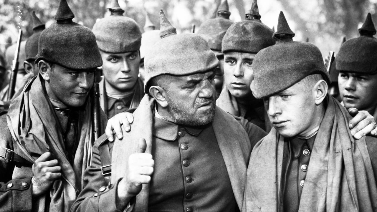 Im Westen nichts Neues (1930), Szenenbild: Nahaufnahme in Schwarz-Weiß: Deutsche Soldaten mit Pickelhaube, in der Mitte steht ein älterer Soldat, der zu einem jüngeren Kameraden spricht.