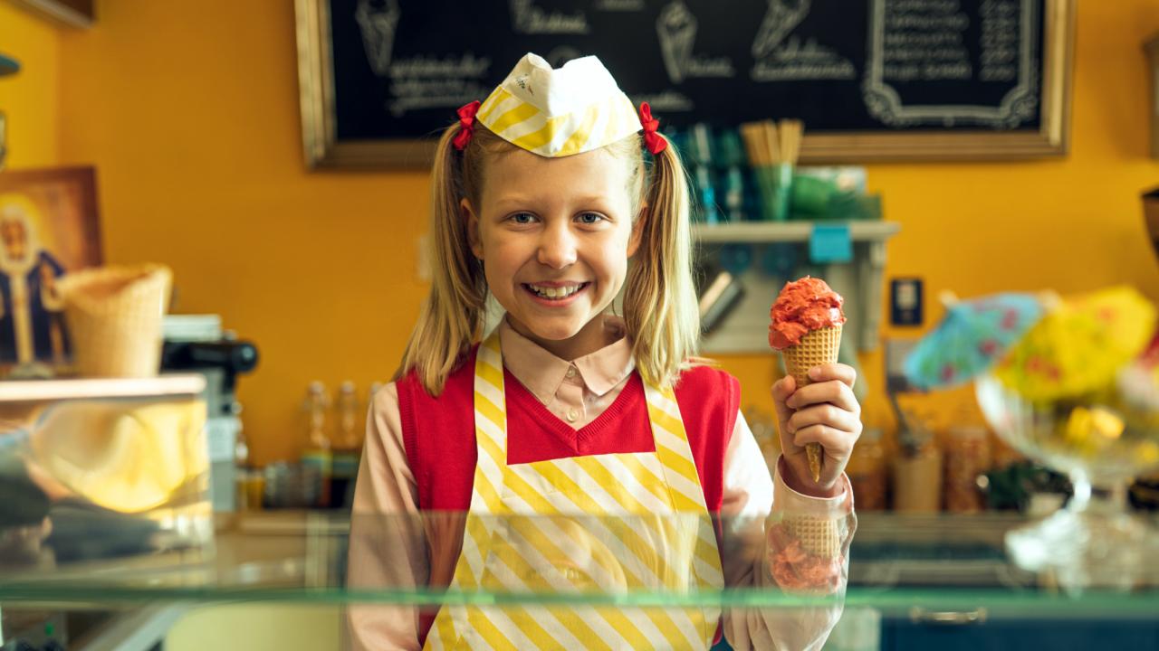 Lucy ist jetzt Gangster, Szenenbild: Ein Mädchen mit Zöpfen und weißer Mütze steht hinter dem Tresen einer Eisdiele und hält lächelnd eine Eistüte in der Hand.