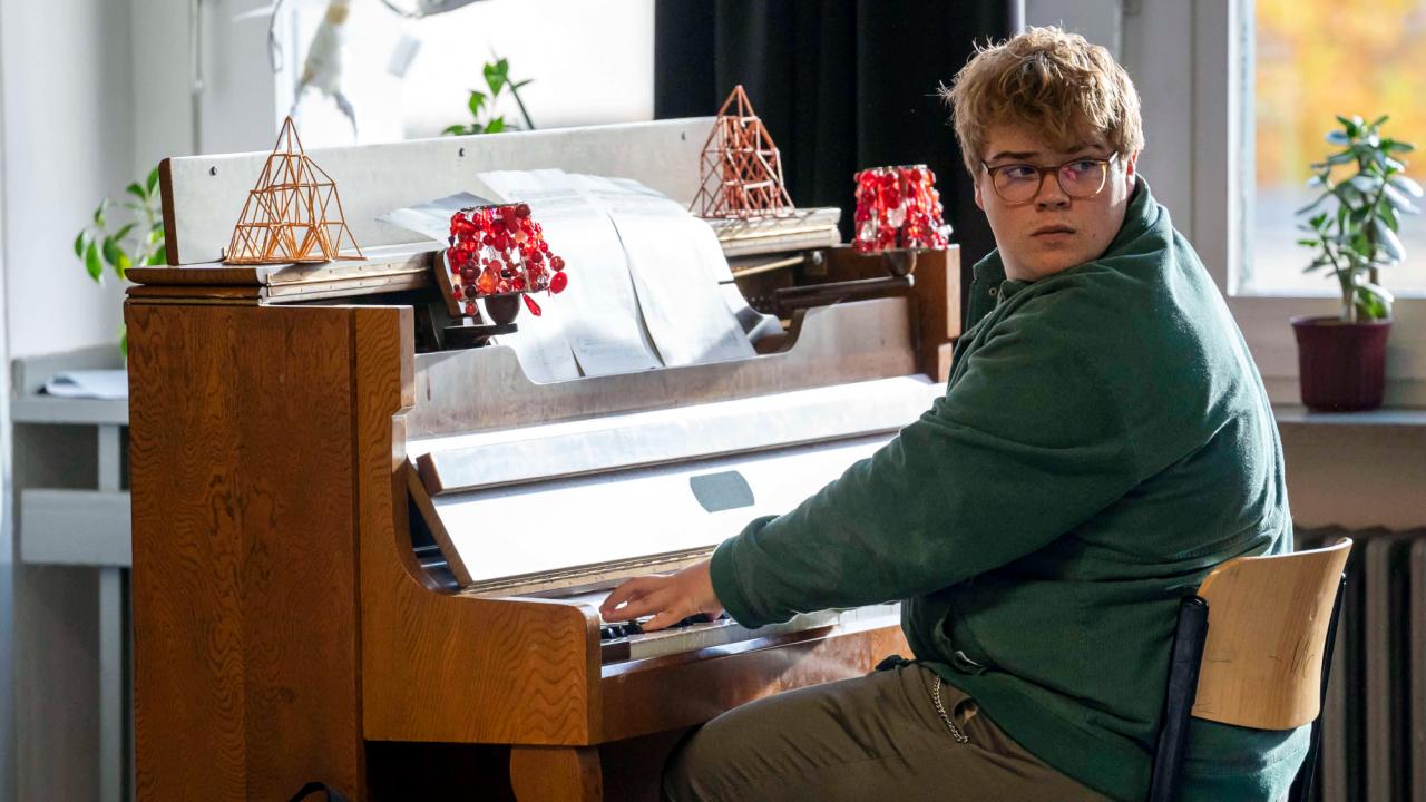 Nackt über Berlin, Szenenbild: Ein junger Mann mit Brille sitzt an einem Klavier und schaut hinter sich.