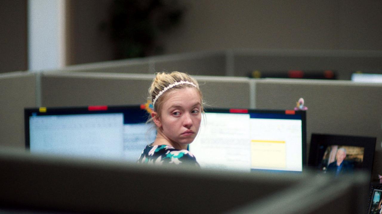 Reality, Szenenbild: Eine junge Frau dreht sitzt an einem Bürotisch mit mehreren Bildschirmen. Sie hat sich umgedreht und blickt sich um.