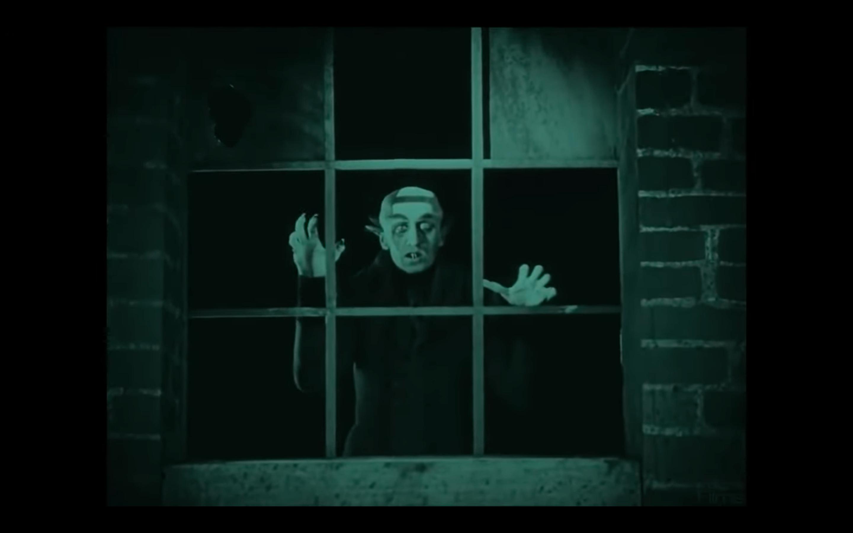 Screenshot aus dem Stummfilm NOSFERATU: Der Vampir Nosferatu blickt durch ein Fenster direkt in die Kamera.