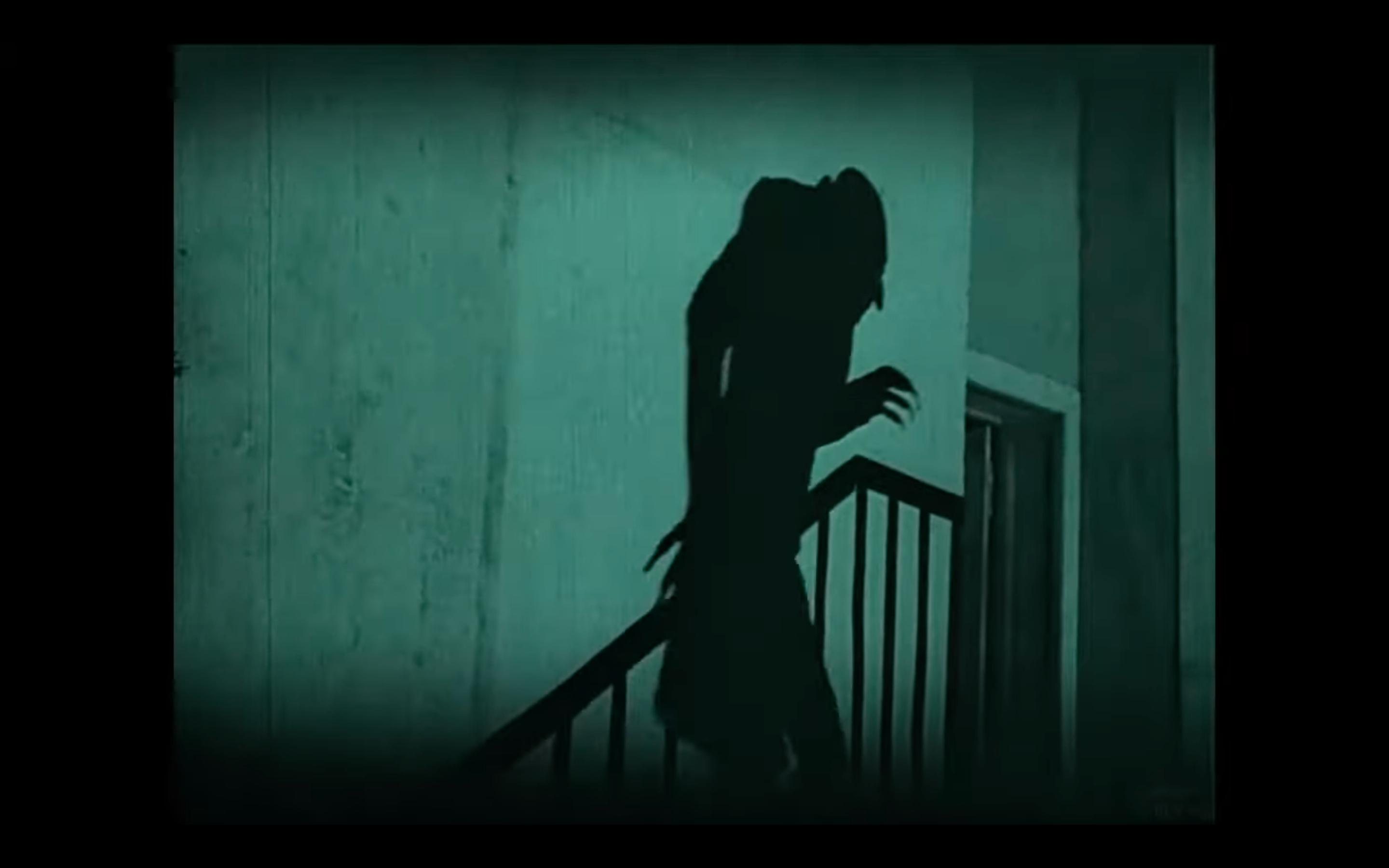 Screenshot aus dem Stummfilm NOSFERATU: An einer Wand ist der Schatten Nosferatus zu sehen, der eine Treppe hinausläuft.