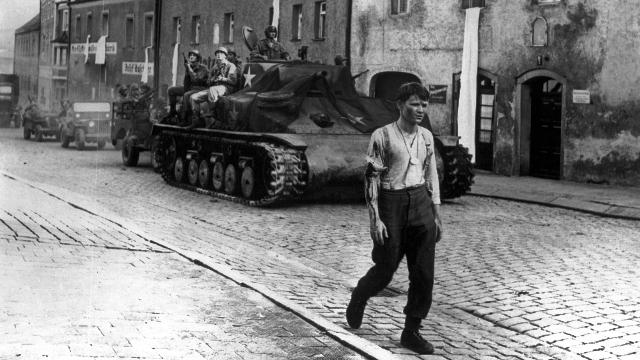 Die Brücke, Szenenbild: Ein junger Mann in Hemd und Uniformhose geht eine Straße entlang. Hinter ihm fährt ein Panzer.