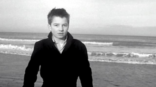 Sie küssten und sie schlugen ihn, Szenenbild: Ein Junge am Strand schaut direkt in die Kamera.